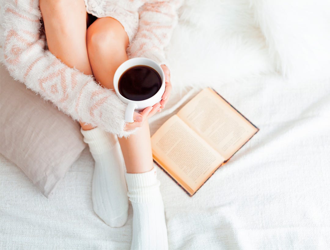 Chica con té en la cama sobre la cama leyendo un libro